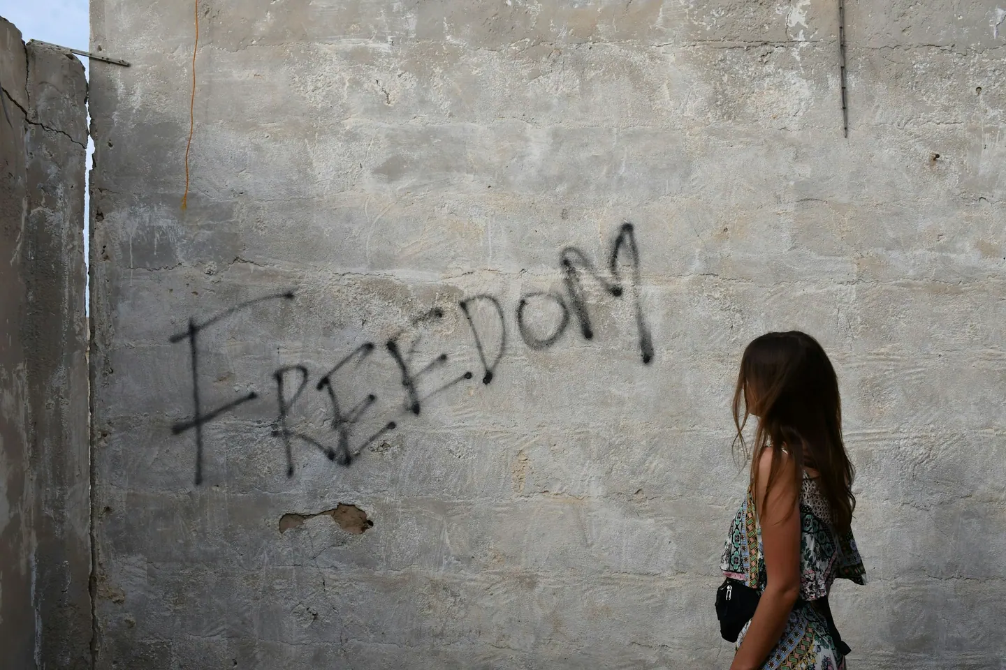 Menina diante de um muro com a palavra freedom (liberdade) pichada
