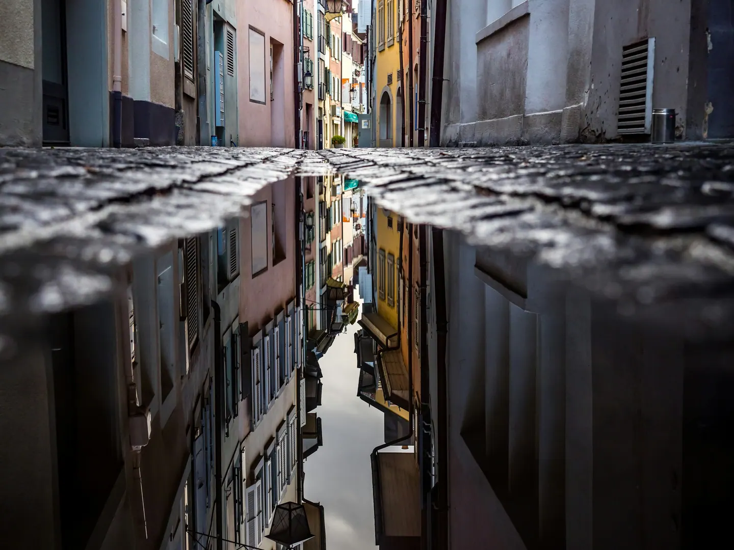 Rua estreita entre casas refletida numa poça de água
